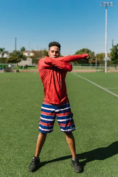 A young male athlete in sportswear stretching and warming up on a sunny soccer field.