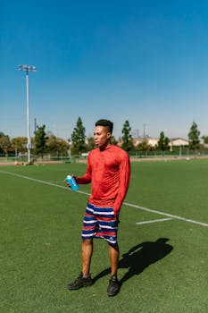 Young athlete rehydrating during outdoor exercise on sunny day at sports field.