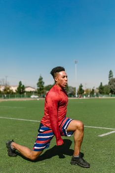 Adult male athlete doing leg stretches on a sunny day outdoors.