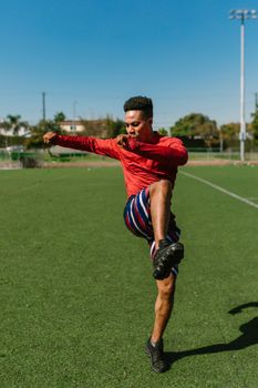Young athlete performing dynamic stretches on a sunny outdoor sports field.