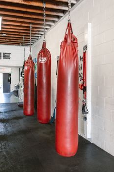 Three red punching bags hang in a well-lit modern gym interior.