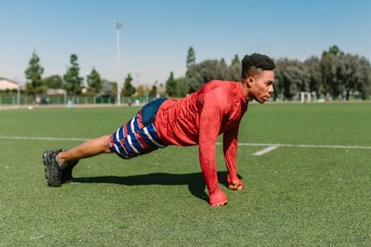 Athletic man doing push-ups on a sunny sports field, capturing outdoor fitness.