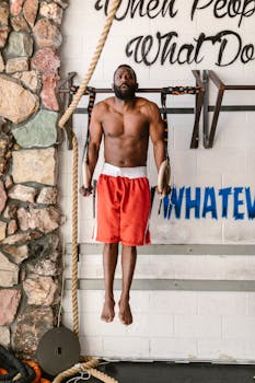 Fit man performs strength workout on gymnastic rings in gym setting, showcasing athleticism.