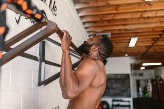 A shirtless man doing a pull-up exercise on a pull-up bar.