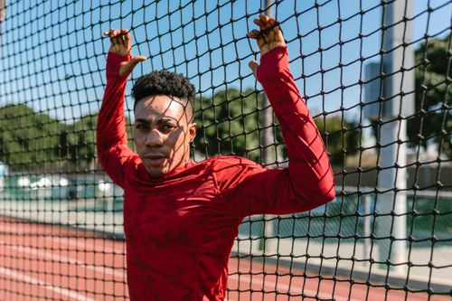 Free An athlete in red sportswear leans on a net on an outdoor track. Stock Photo