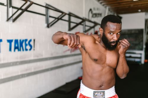 Free Muscular African American man practicing boxing in a gym setting, showing focus and determination. Stock Photo