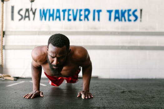 A man in a gym doing push-ups with a motivational quote on the wall behind him.