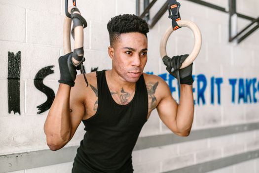 A determined athlete strength-training on gymnastic rings at an indoor gym, emphasizing fitness and focus.