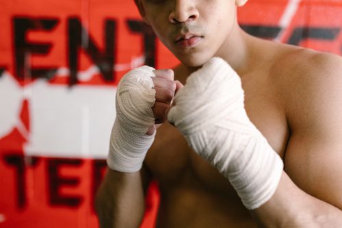 Free A focused boxer with clenched fists and hand wraps prepares for a match against a striking red background. Stock Photo