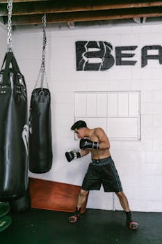 Fit young man boxing with gloves in an indoor gym setting, showcasing strength and focus.