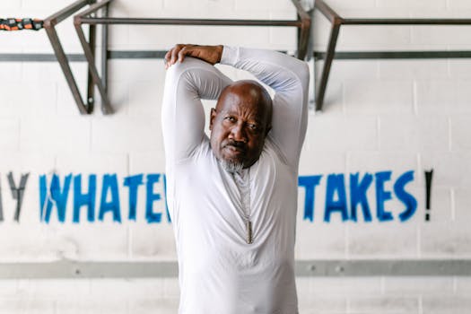 Middle-aged man performs arm stretch indoors in a motivating gym environment.