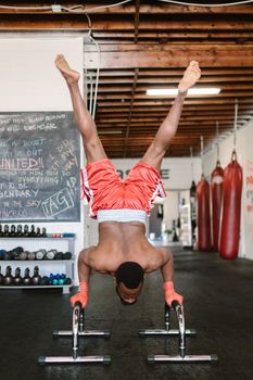 Man doing handstand on bars in a boxing gym, showcasing strength and balance.