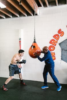 Boxer practicing punches on a speed bag with a coach's guidance in a gym environment.