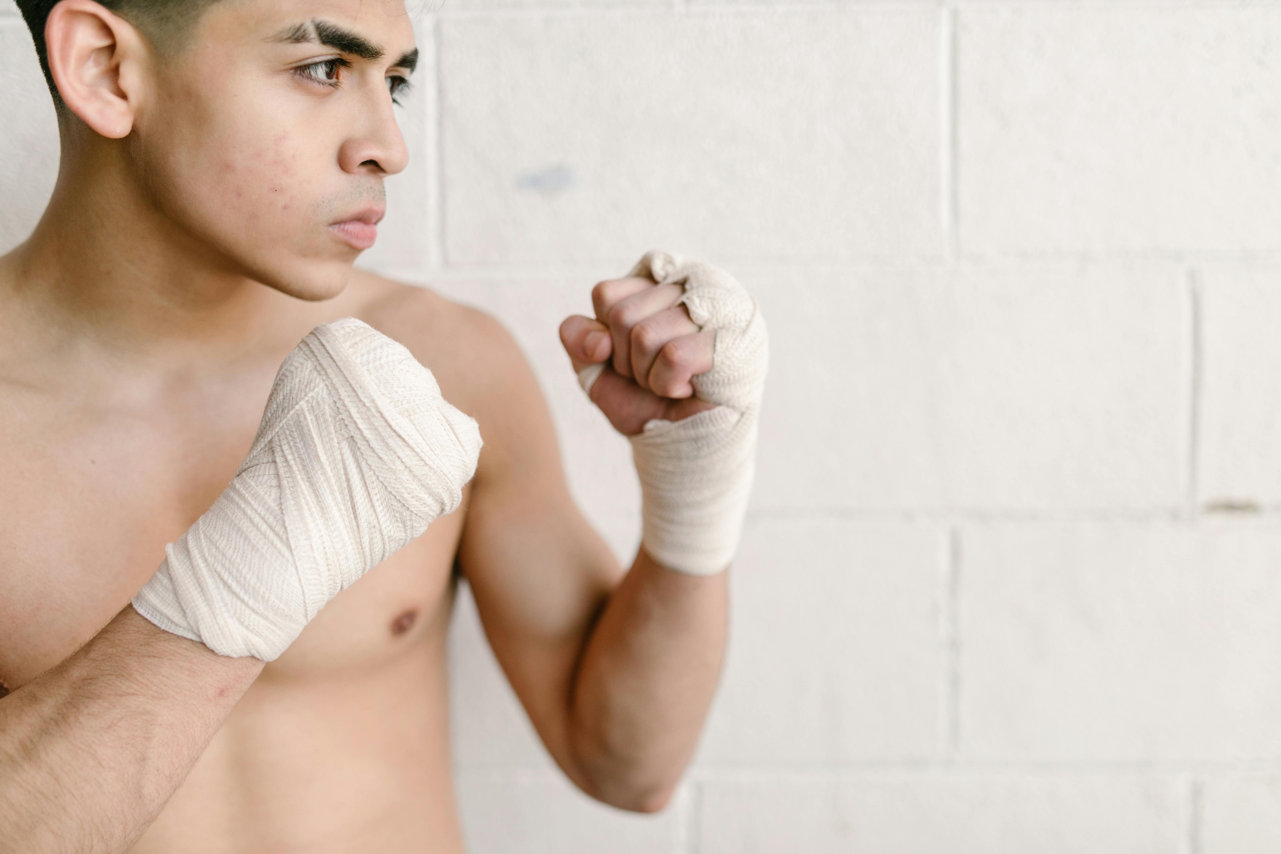 Focused young male boxer with hand wraps in fighting stance, ready for training. — photo by RDNE Stock project