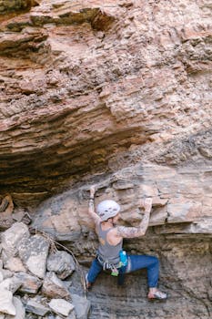 A woman rock climber skillfully ascends a natural rock formation using climbing gear, showcasing outdoor adventure.