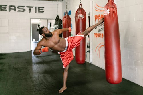 Shirtless Man Kicking a Punching Bag