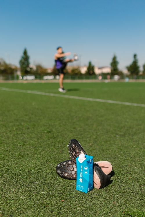Free Close-up of soccer cleats and an energy drink with player in background on sports field. Stock Photo