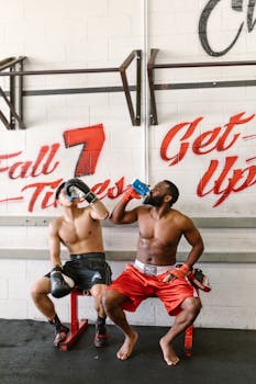 Two boxers resting and hydrating in a gym with motivational graffiti.