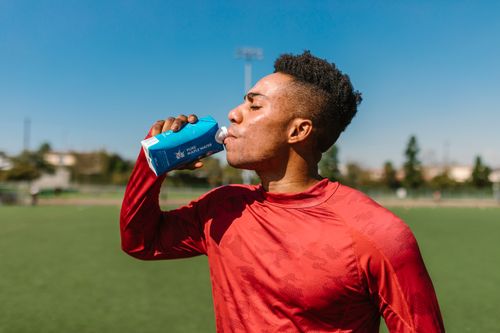Free Adult athlete in a red shirt drinking water outdoors on a sunny day after sports activity. Stock Photo