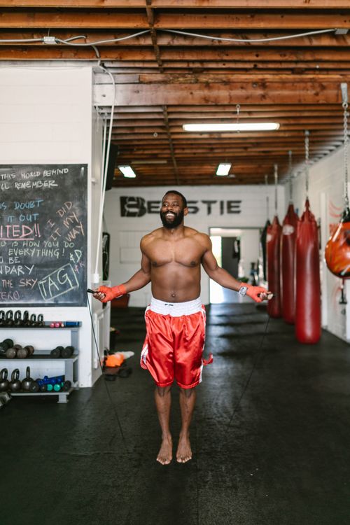 Free African American man jumping rope in a boxing gym, shirtless and wearing red shorts, showing fitness and agility. Stock Photo