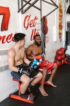 Two boxers take a break in a boxing gym, showcasing camaraderie and training intensity.