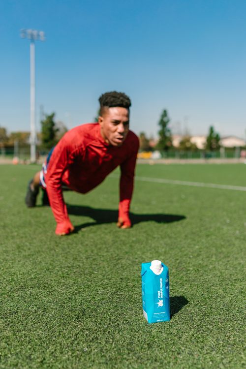 Free Athletic man exercising outdoors in sunlight, focused on a carton of drink. Stock Photo