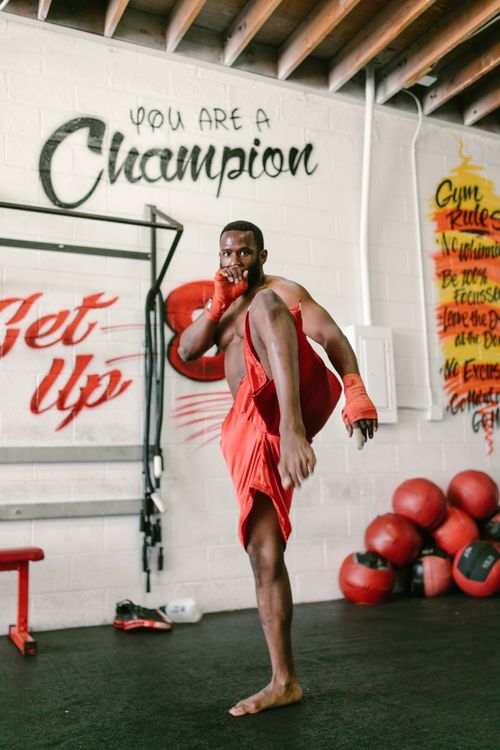 Free A shirtless, muscular man performs a high kick in a gym with motivational wall graffiti. Stock Photo
