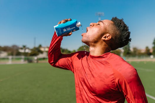 An athlete in a red shirt hydrates with maple water on a sunny day outdoors.