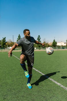 An athlete practicing soccer skills on a green field under a clear blue sky.