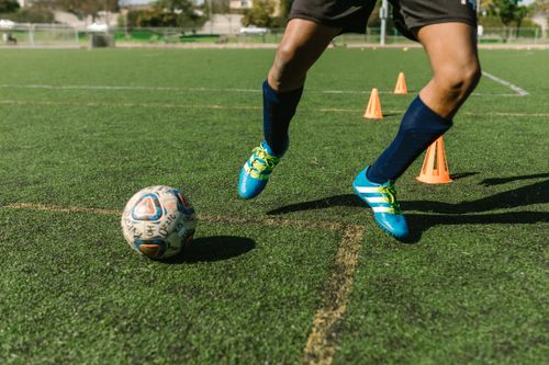 Free Dynamic image of a soccer player practicing drills on a grass field with vibrant shoes and cones. Stock Photo