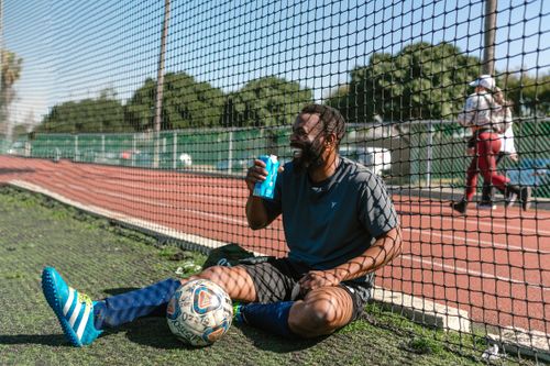 Free Smiling soccer player taking a break with a drink on the sports field. Stock Photo