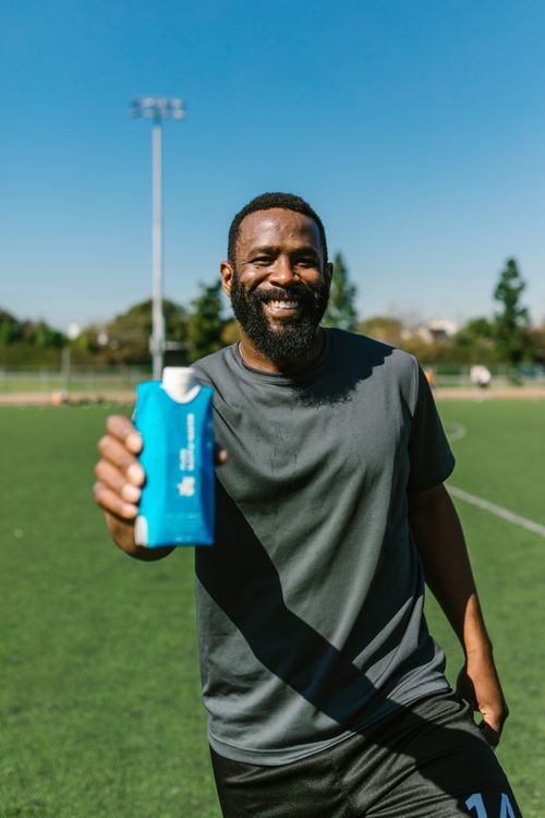 Free Bearded man smiling while holding a water bottle on a sunny soccer field. Stock Photo