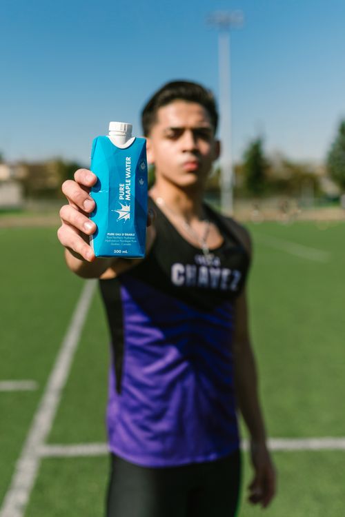 Free A young athlete presenting Pure Maple Water during a sunny day on a sports field. Stock Photo