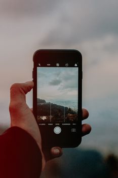 Smartphone held by hand capturing a scenic landscape view, showcasing photography on mobile devices.