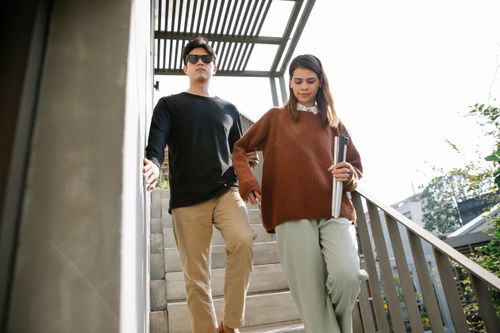 Free Two young adults walk downstairs with sunlight casting shadows. Casual scene outdoors. Stock Photo