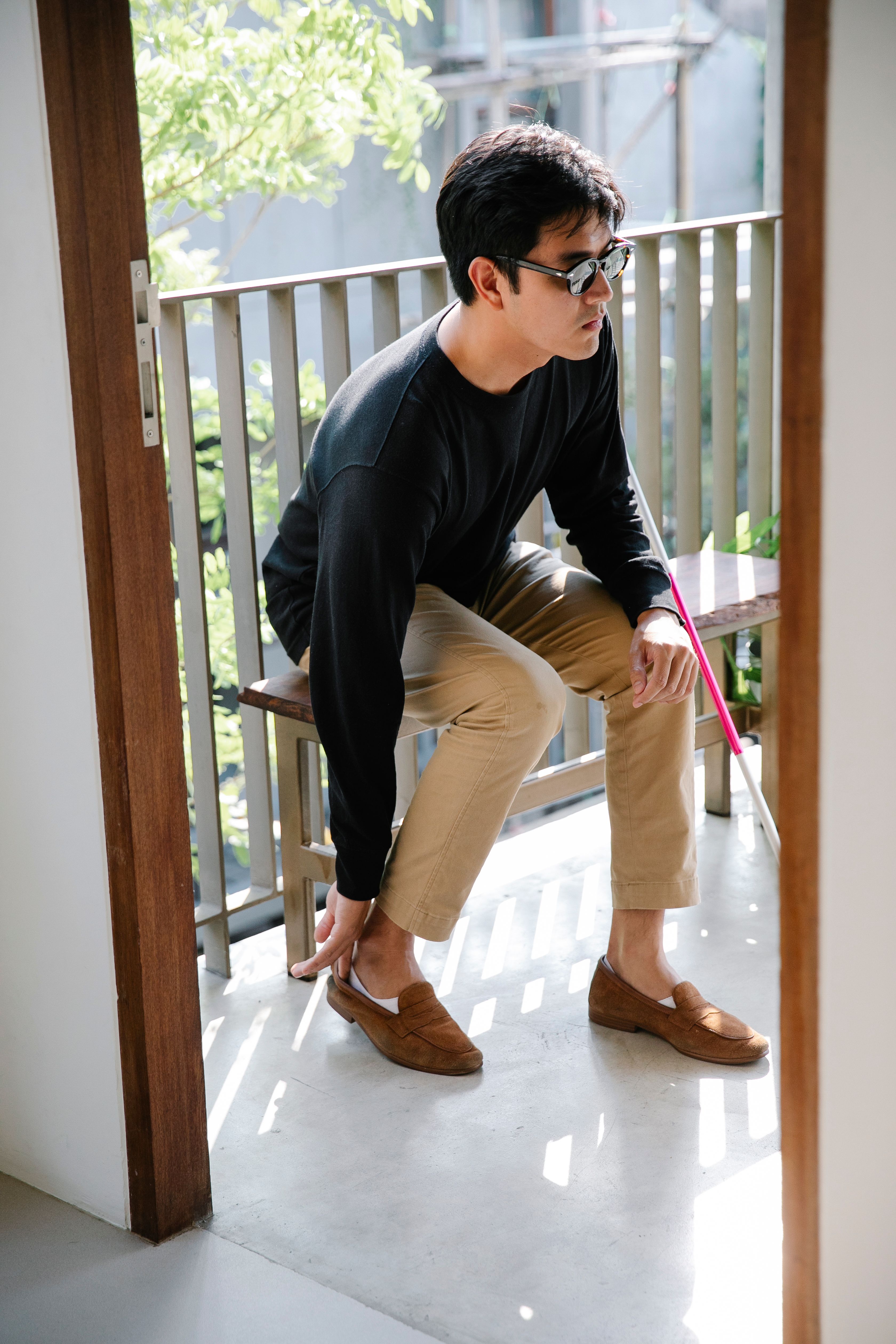 An adult man with visual impairment sits on a bench putting on shoes, embodying independence.