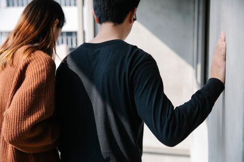Free A casual couple standing together, facing a wall on a sunny day. Stock Photo