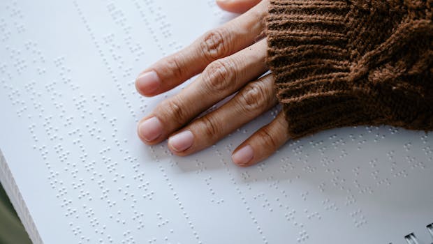 A hand gently reads Braille text on paper, emphasizing touch and inclusivity.