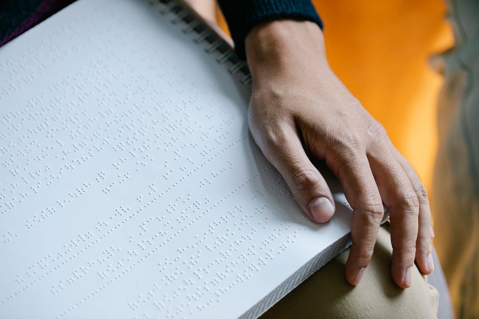 A hand touching a Braille book in a close-up shot, highlighting tactile reading.