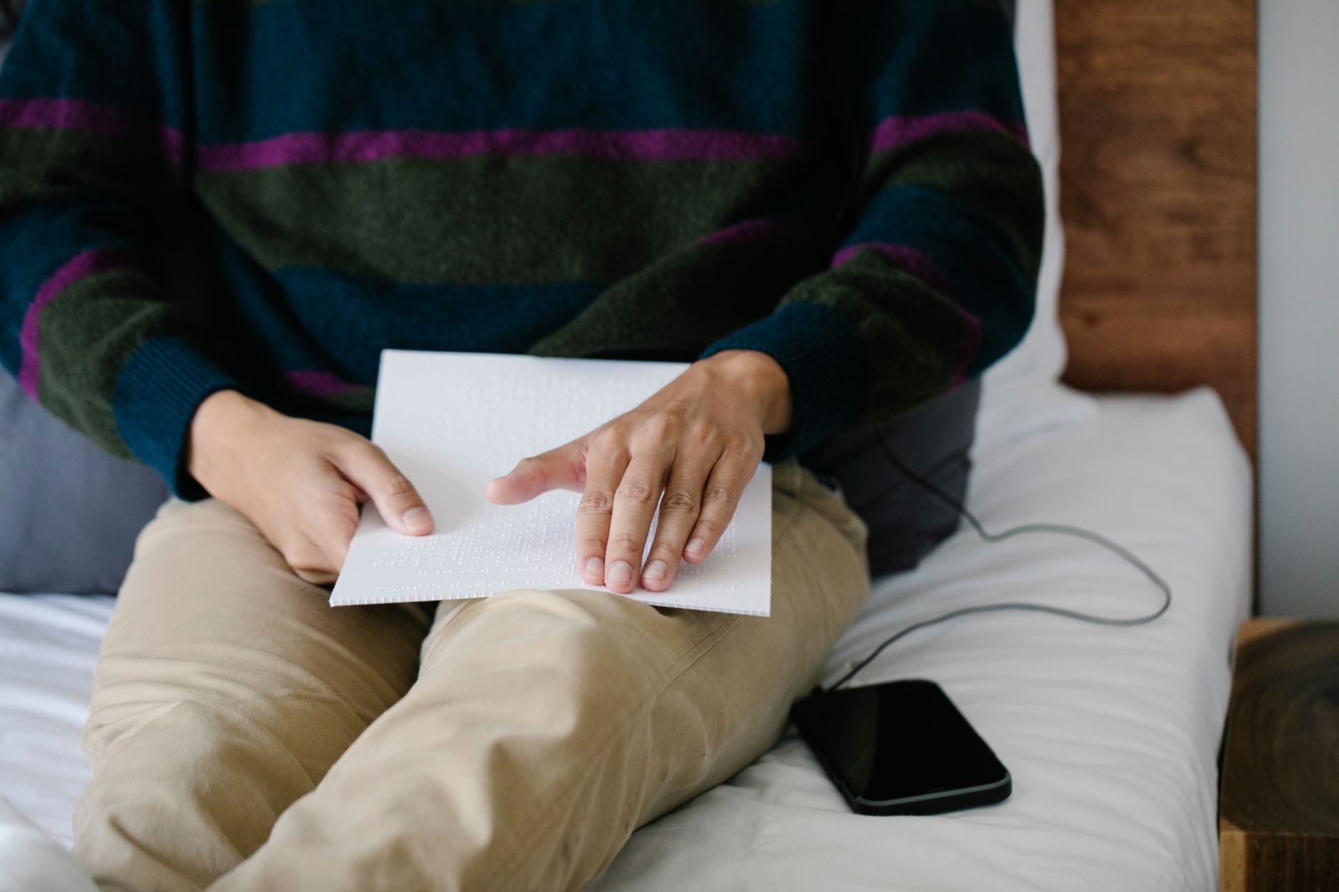Adult reading braille in a casual setting with smartphone nearby, enhancing sensory education.