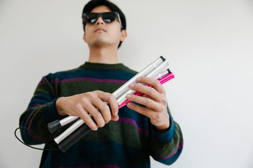 Free Portrait of a man with sunglasses holding a collapsible walking stick, emphasizing independence. Stock Photo