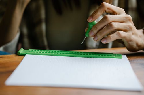 Free A hand using a stylus to write on a Braille slate on a desk. Stock Photo