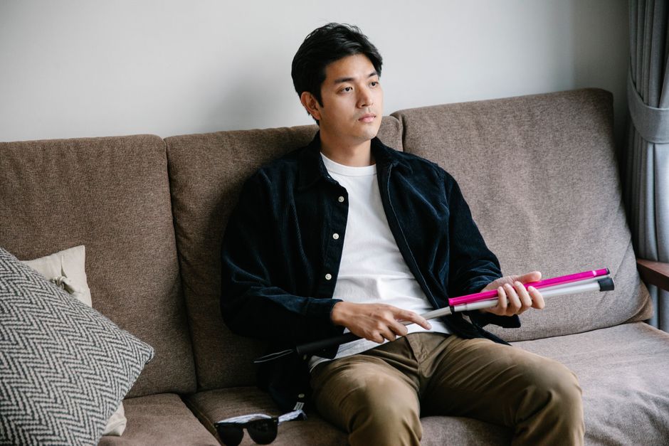 白い杖を持った男性が茶色いソファに考え込んで座っており、独立と熟考を象徴しています。