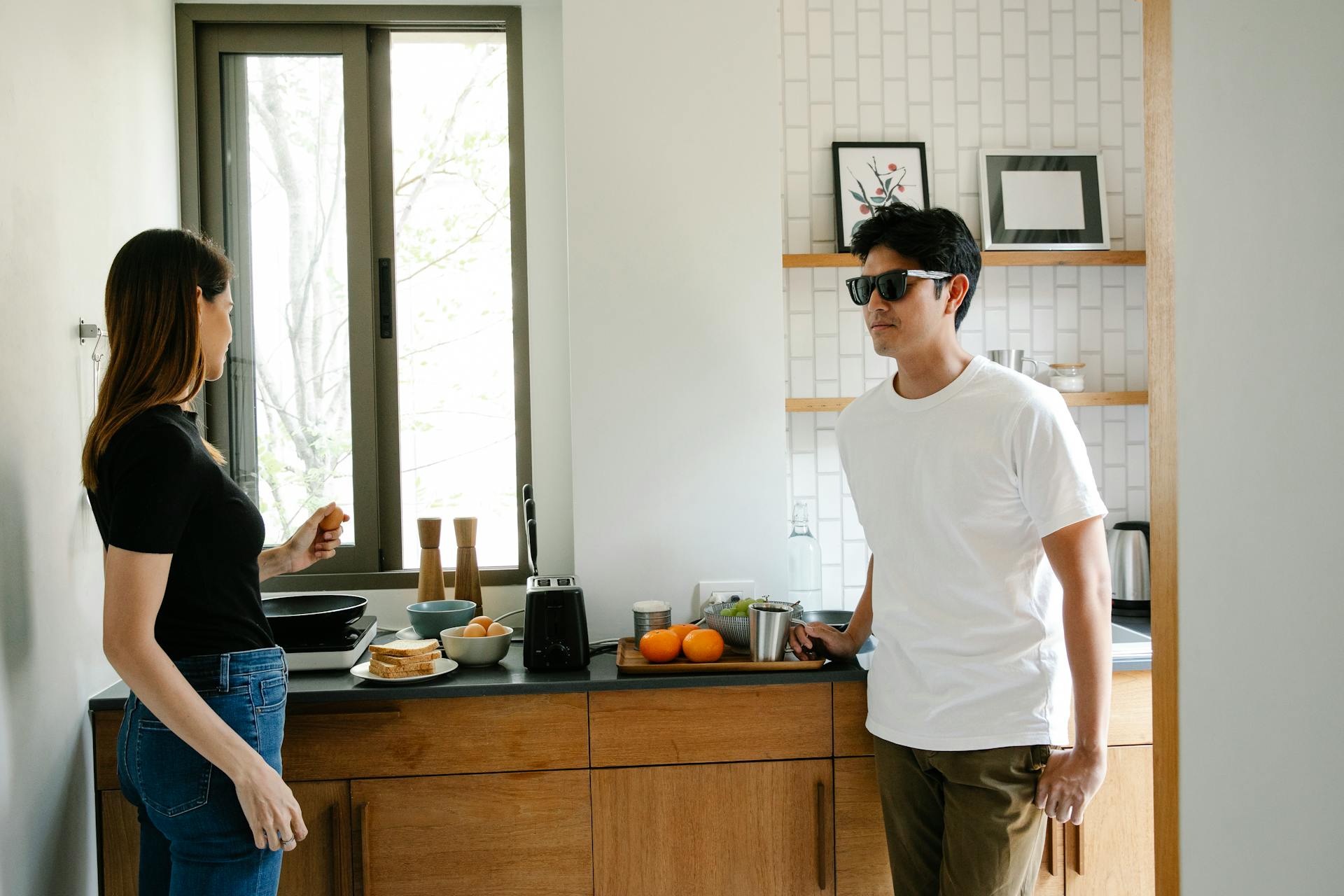 Young Asian man with vision loss in black glasses standing in kitchen with wife preparing breakfast while spending morning together at home