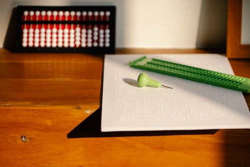 Free Close-up of Braille paper with stylus and abacus on a sunlit wooden desk, highlighting tactile learning tools. Stock Photo