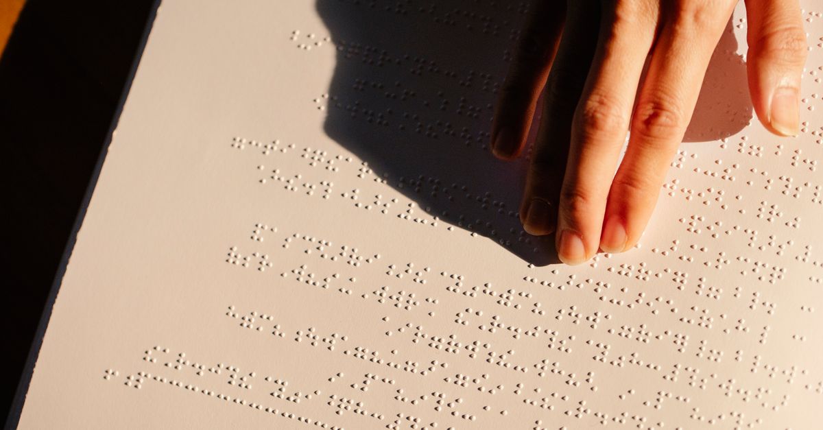 A close-up of a hand feeling and reading Braille text on paper under soft lighting.