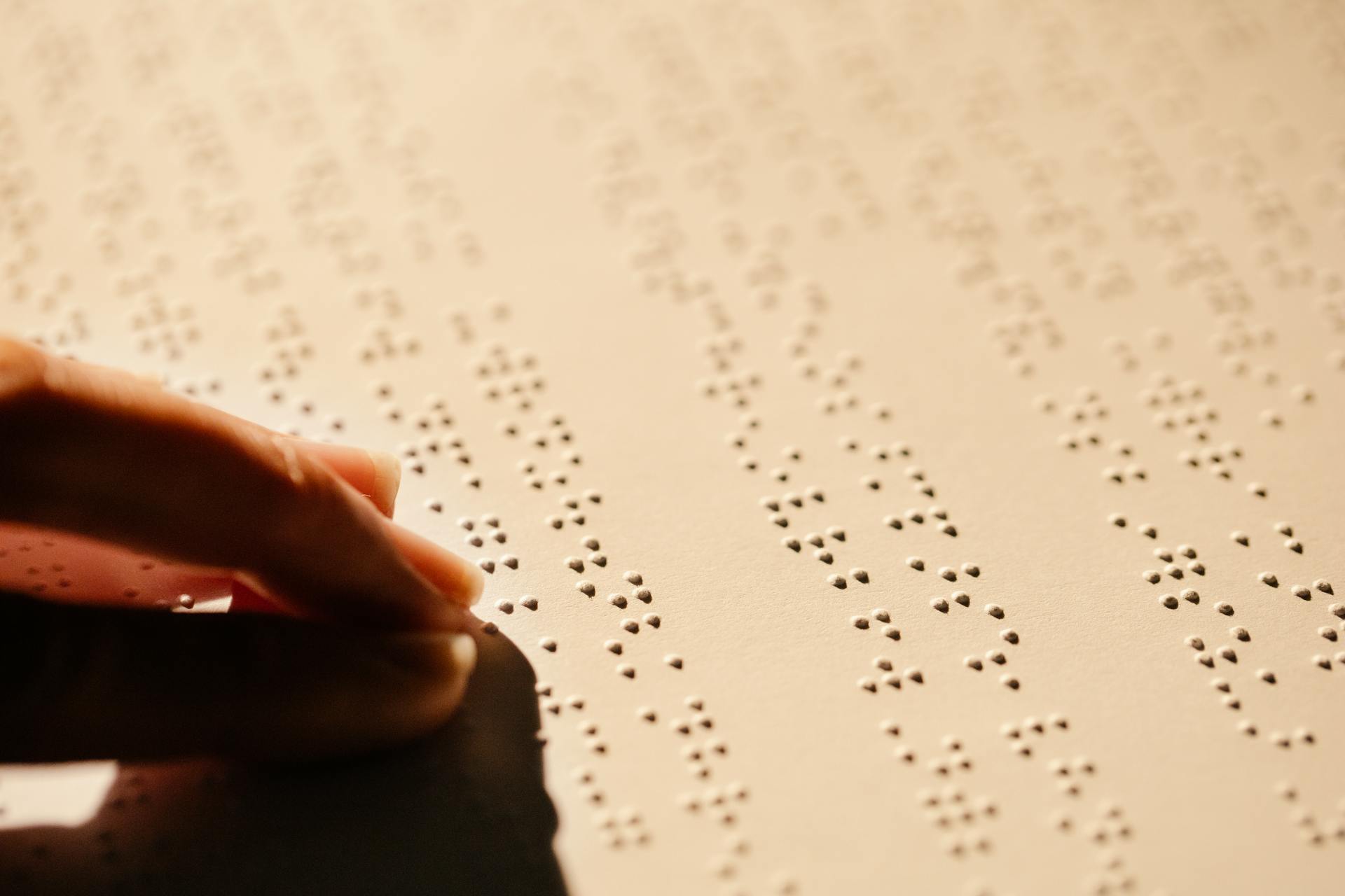 A close-up image of a hand touching embossed Braille text on a paper sheet, highlighting tactile reading.