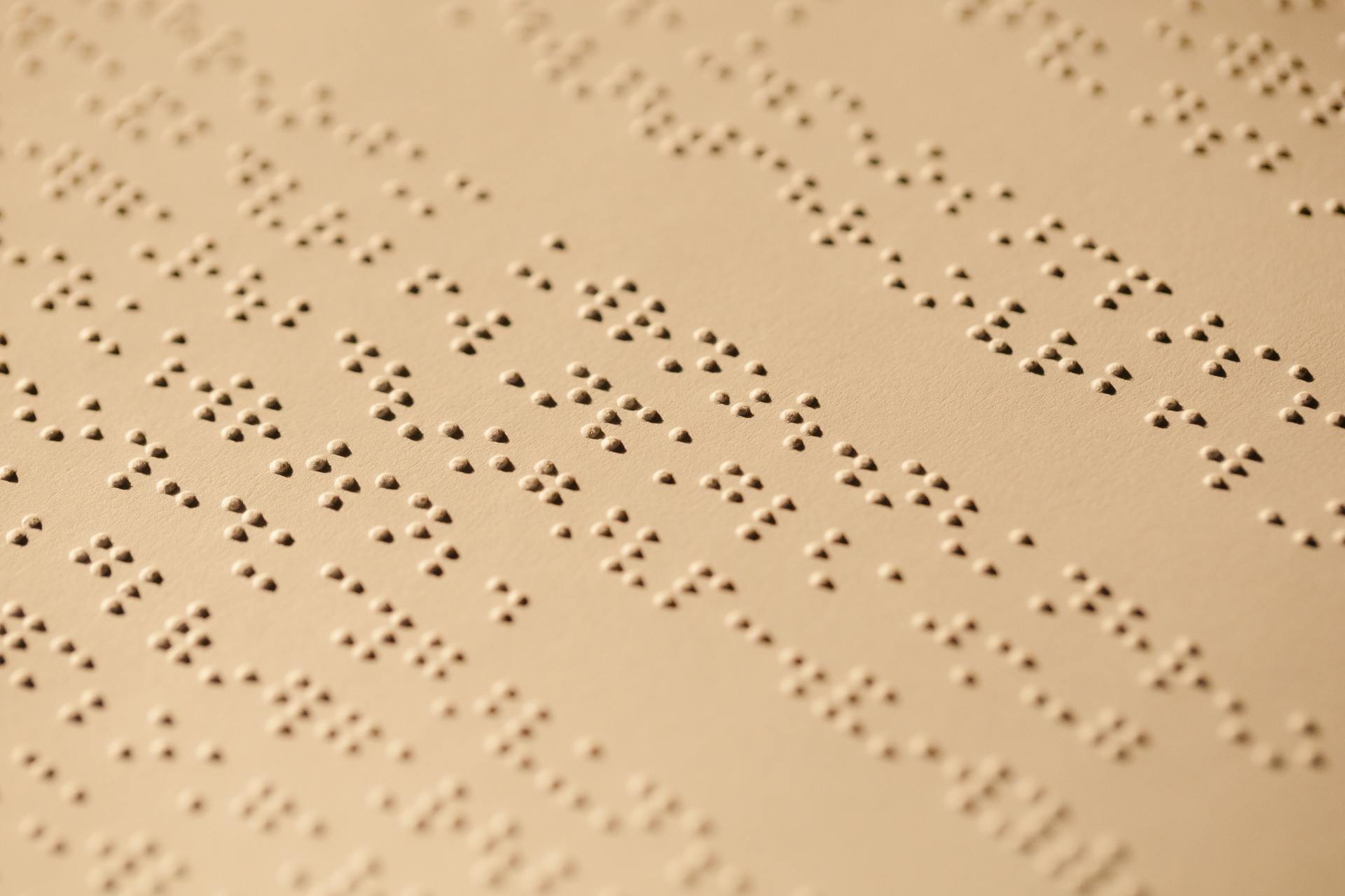 Detailed close-up of Braille text embossed on a beige textured paper surface.