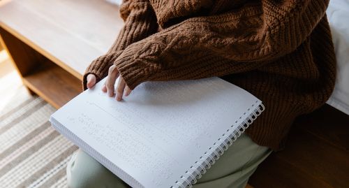 Free A person in a knitted sweater reads a Braille book, emphasizing sensory perception and tactile learning. Stock Photo