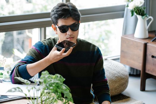 A man wearing sunglasses uses a smartphone's voice assistant in a cozy indoor setting. - Fotografer Sidoarjo